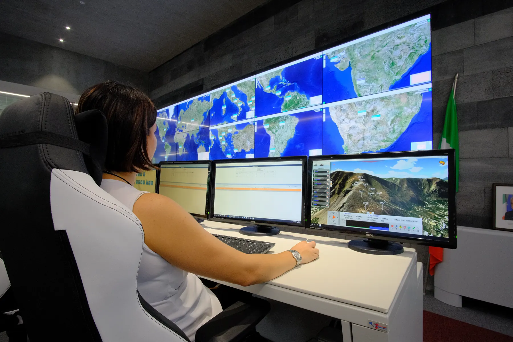 Operator at a monitoring desk in front of a video wall showing satellite maps