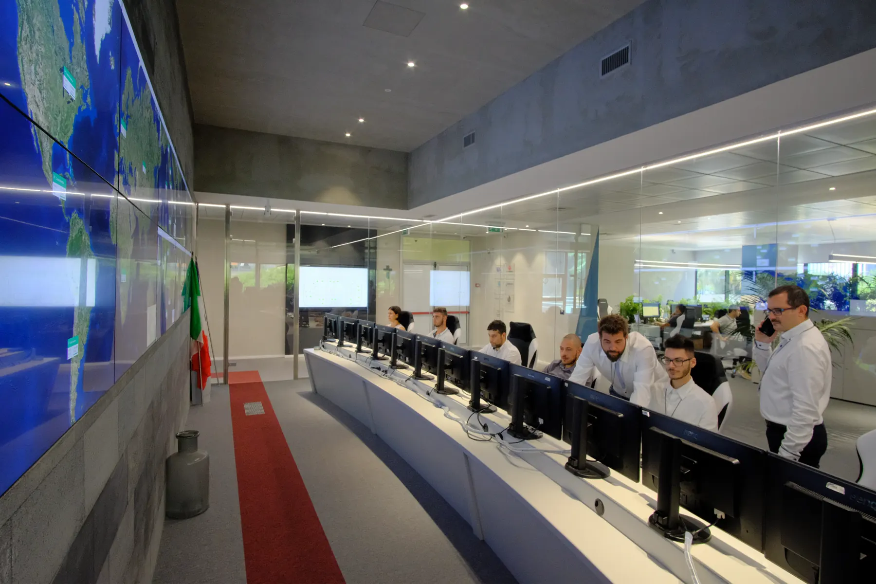 Control room with a curved desk of monitors and a wall of world maps